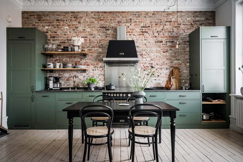 Geweldige keuken met groene keukenkasten en bakstenen keuken achterwand. Wel is er ook gekozen voor een RVS spatwand achter het fornuis, passend bij het fornuis en afzuigkap.