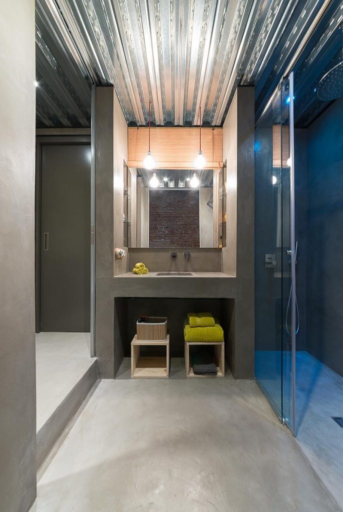 Deze stoere industriele badkamer is ontworpen door Studio FFWD, die betonlook wanden, vloer én wastafel gecombineerd hebben met een plafond van golfplaten en stoere industriële hanglampen. | Fotografie: David Benito Cortázar