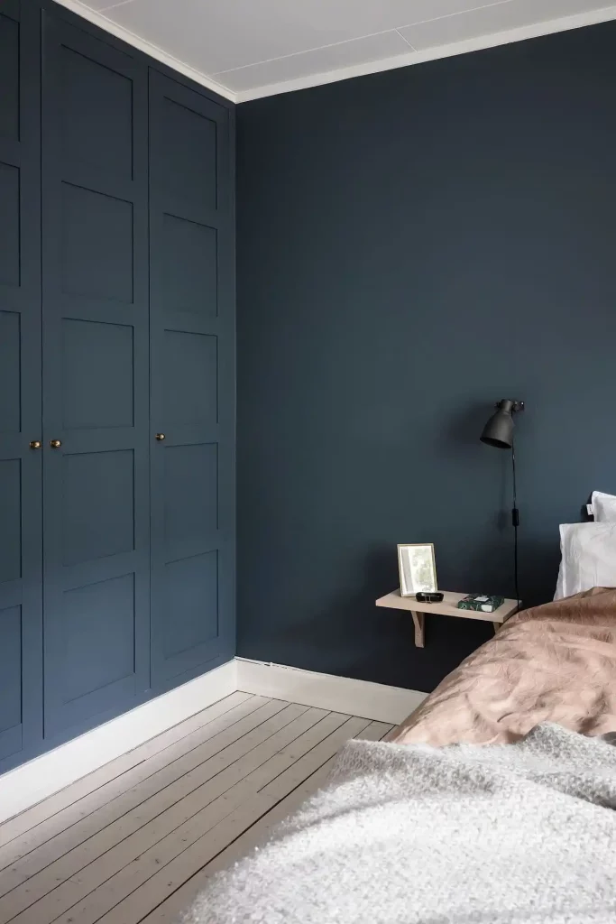 In deze fijne slaapkamer is de kledingkast op maat in dezelfde tint blauw geverfd als de muren. De houten vloer en het houten nachtkastje staan er geweldig bij.