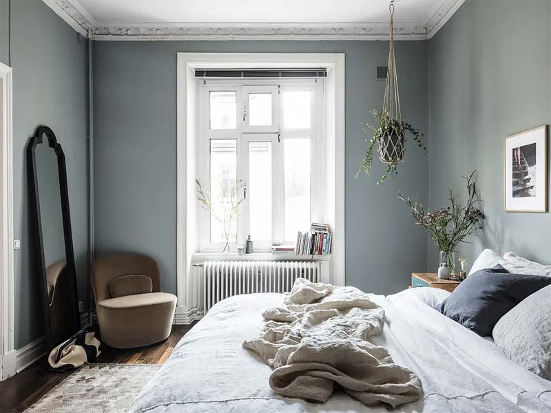 In deze slaapkamer met blauwe muren en houten vloer, is er gekozen voor een stijlvolle fluwelen fauteuil in een mooie bruine accentkleur. 