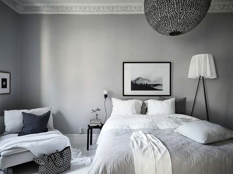 In deze mooie Scandinavische slaapkamer, met vooral de kleuren wit en grijs, is een bijpassend fauteuil gekozen naast het bed die perfect erin past.