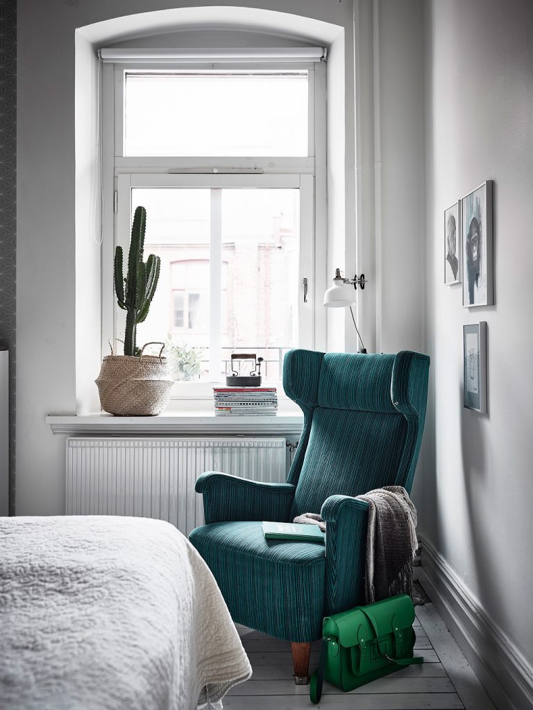 De klassieke fauteuil in de hoek van deze slaapkamer is leuk gedecoreerd met een deken, lijsten aan de muur, een wandlamp en vensterbank decoratie.