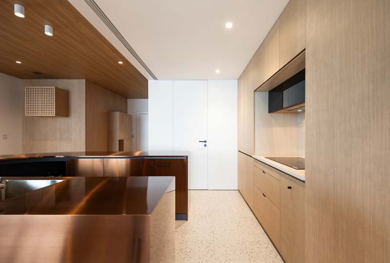 DaoHo Studio heeft in dit mooie moderne appartement gekozen voor een strakke witte blinde deur in de keuken, dat een mooi geheel vormt met de witte muur.