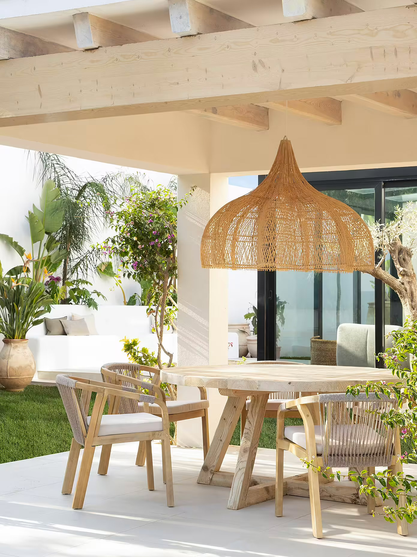 De ontwerpers van Susanna Cots Interior Design hebben in deze Ibiza tuin gekozen voor een grote geweven hanglamp boven een ronde eettafel. | Fotografie: Mauricio Fuertes