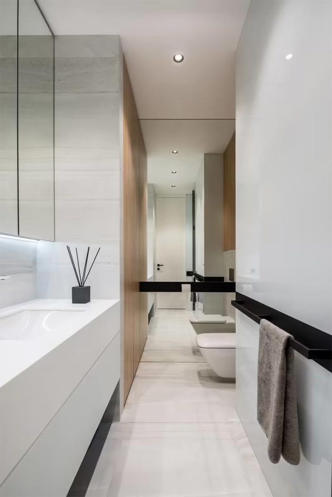 Deze moderne badkamer is ontworpen door Mono Architects. Naast een zwevende badkamer op maat, is er ook een grote inbouwkast gecreëerd tegenover het toilet.