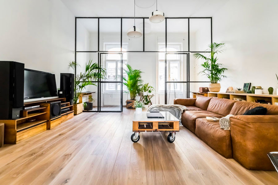 Deze woonkamer heeft een stoere industriële look gekregen, onder andere door de cognac leren bank én de grote glazen wand met stalen kozijnen en dubbele stalen deuren.