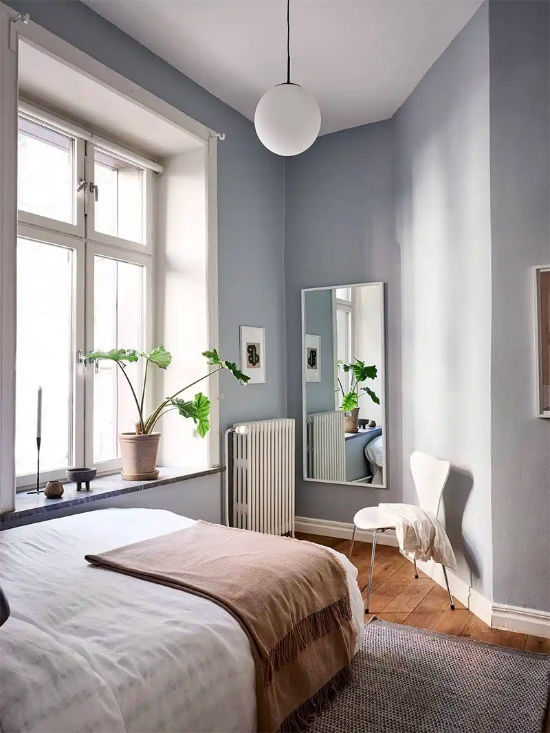 In deze frisse kleine slaapkamer met blauwe muren, is de grote spiegel op een strategische plek opgehangen.