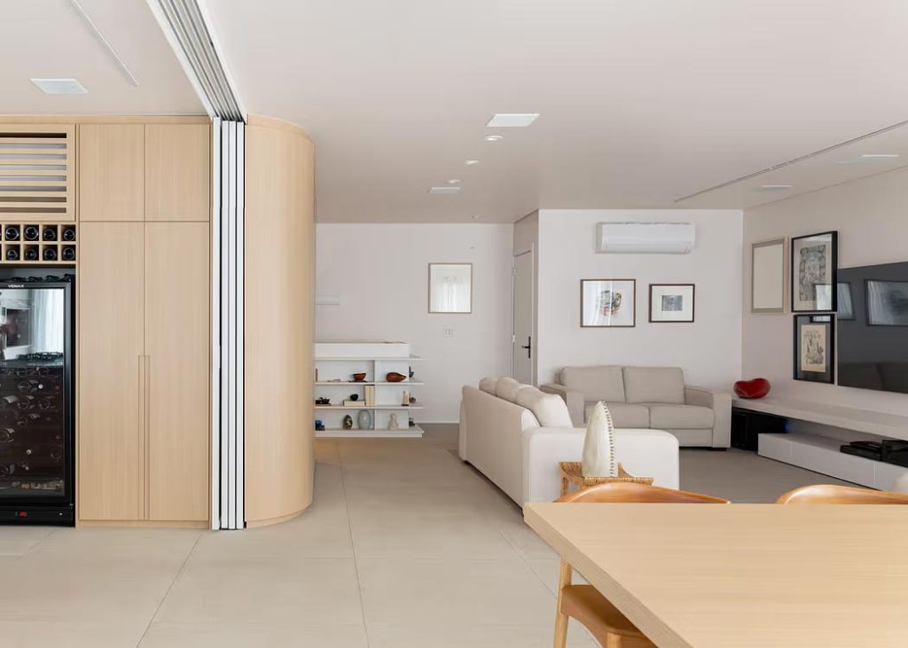 In deze l-vormige woonkamer, ontworpen door Nommo Arquitetos, zijn schuifwanden geplaatst, waarmee de open keuken volledig gescheiden kan worden van de zithoek en eethoek.