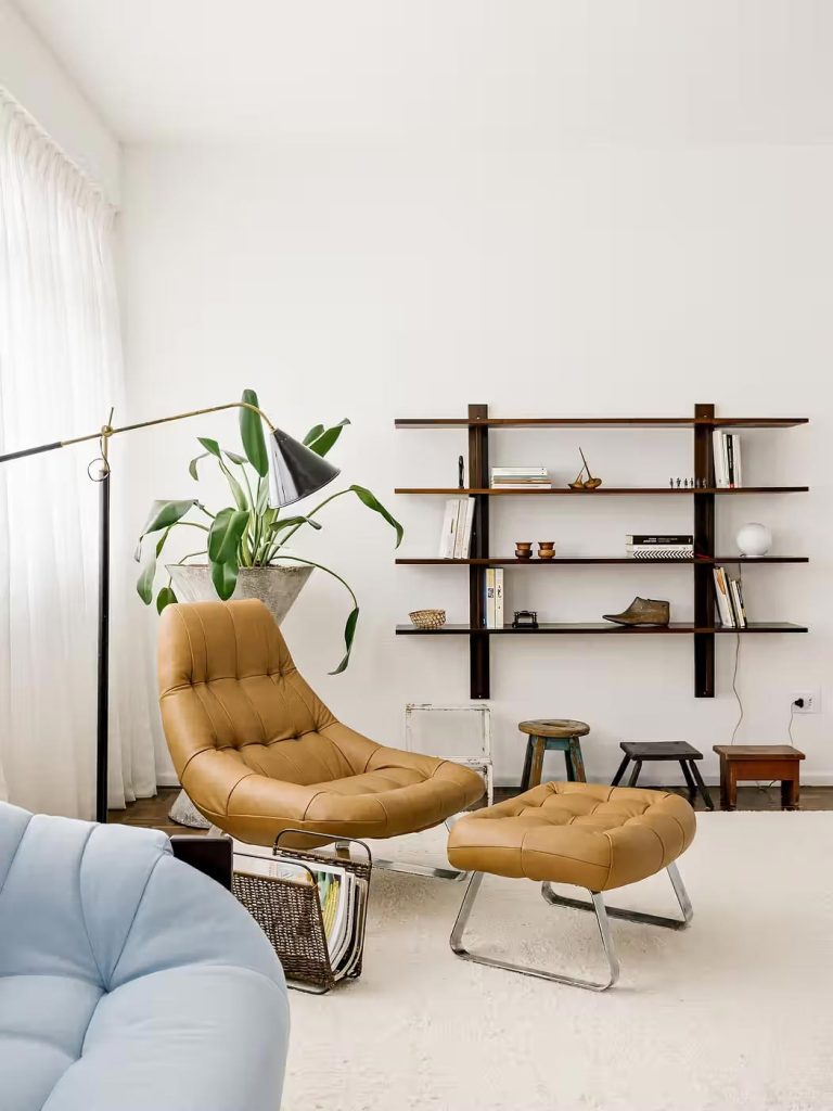 In de woonkamer is ook een leuke zithoek gecreeerd met een super mooie bruine leren lounge chair en bijpassende houten wandrek. | Fotografie: Fran Parente
