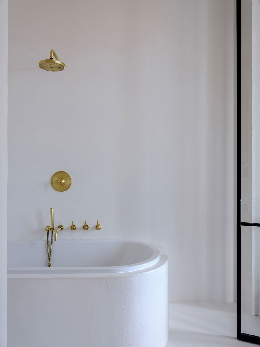 luxe badkamer ensuite met witte pleisterwanden, gouden kraan en gouden douche
