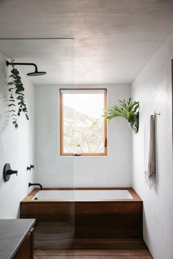 De minimalistische badkamer van Erin, met een houten bad en stijlvolle wandplanten aan de gestuukte muren. Klik hier voor meer foto's.