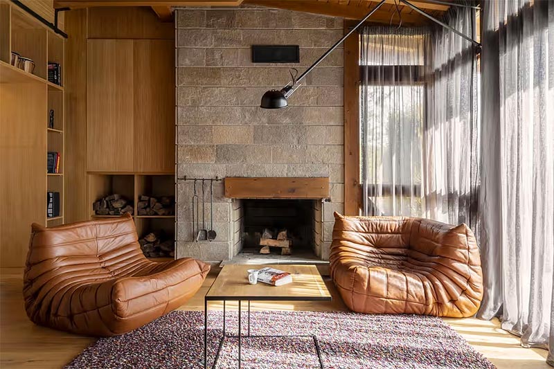 In deze knusse rustieke woonkamer heeft Makeroom Architects een mooie houten inbouwkast ontworpen met open vakken voor het opbergen van stapels hout.
