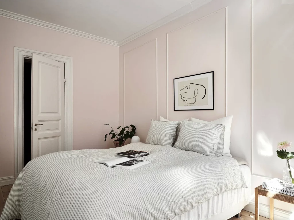 Chique slaapkamer met pastelroze muren, die gedecoreerd zijn met sierlijsten.