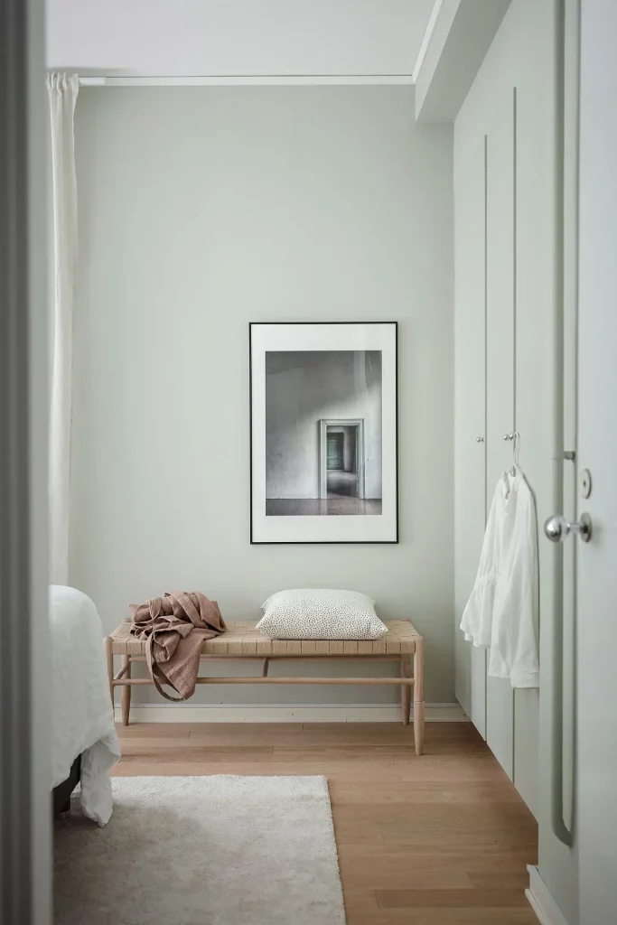 De grote kledingkast is in dezelfde mintgroene kleurtint geschilderd als de pastelgroene muren in deze frisse slaapkamer.