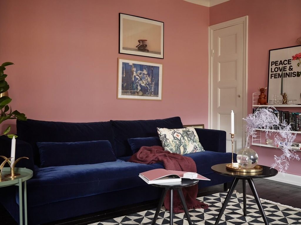 Een fluwelen blauwe bank en roze muren vormen een chique look in deze woonkamer.