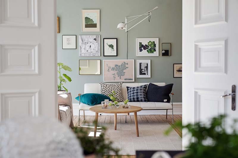 De sage green muur overheerst in deze woonkamer vol met andere leuke kleuren.