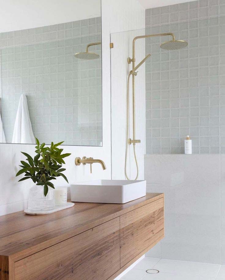 Frisse badkamer met combinatie van witte en sage green tegels, houten badkamermeubel en gouden kranen en douche.