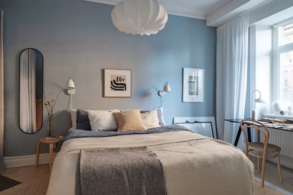 In deze kleine slaapkamer zijn de lichblauwe muren gecombineerd met lichte neutrale tinten, zoals de lichtbeige bedsprei en de witte gordijnen.
