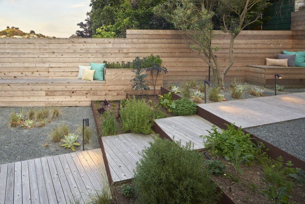 In deze mooie moderne tuin met niveauverschillen, zijn moderne tuinpalen met verstelbare spotjes langs de met houten vlonders beklede trap geplaatst.