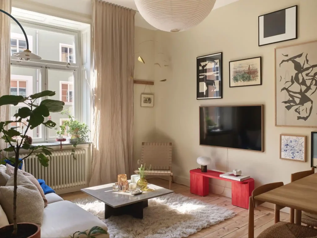 In deze mooie woonkamer met beige muren is de TV aan de muur onderdeel van een collage met lijsten.