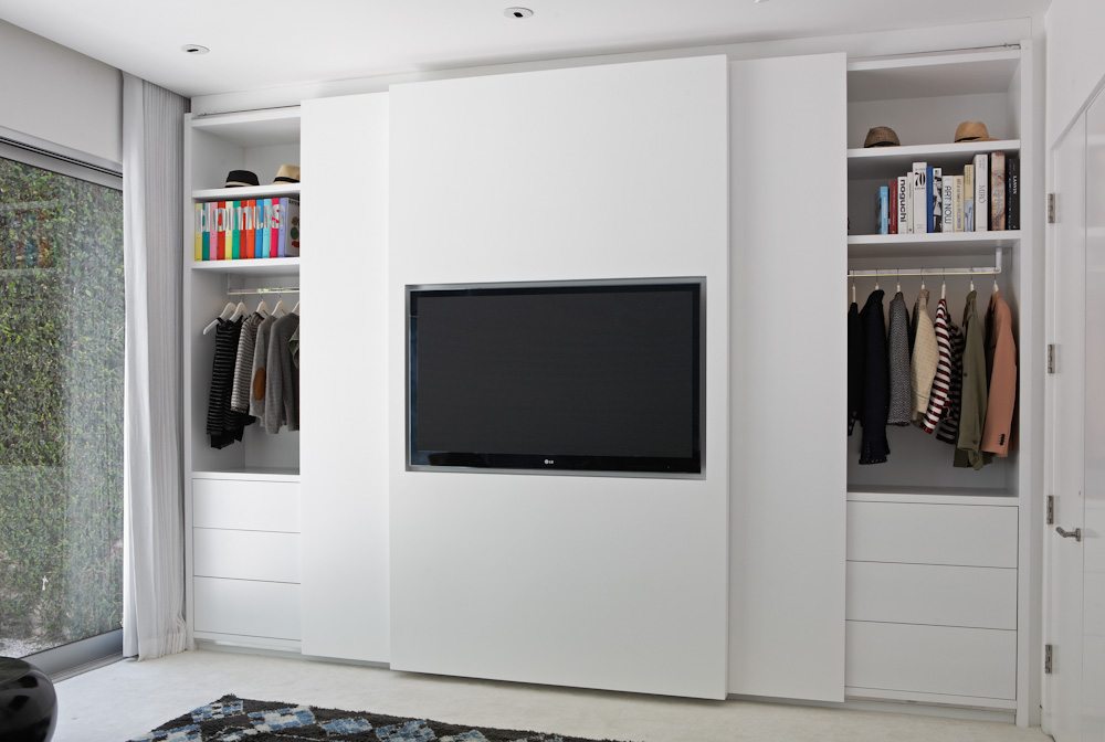 La Closet Design heeft een op maat gemaakte kast ontworpen, waar de TV aan de schuifdeur opgehangen kan worden in een moderne slaapkamer.