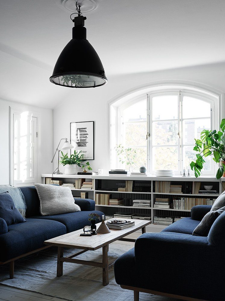 In deze mooie Scandinavische woonkamer zijn twee identieke blauwe banken tegenover elkaar geplaatst, gescheiden door een rechthoekige salontafel.
