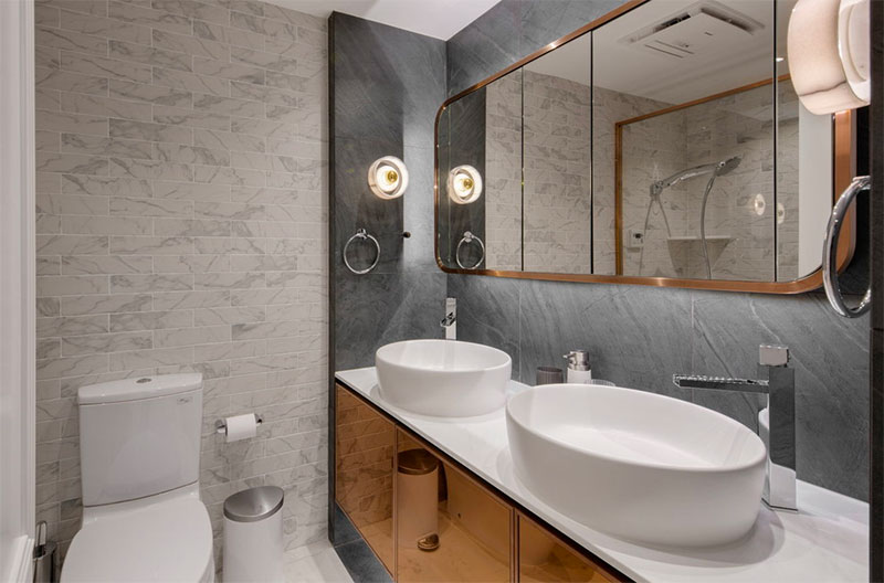 In deze kleine badkamer met een laag plafond is er gekozen voor mooie wandlampen bij de dubbele wastafels.