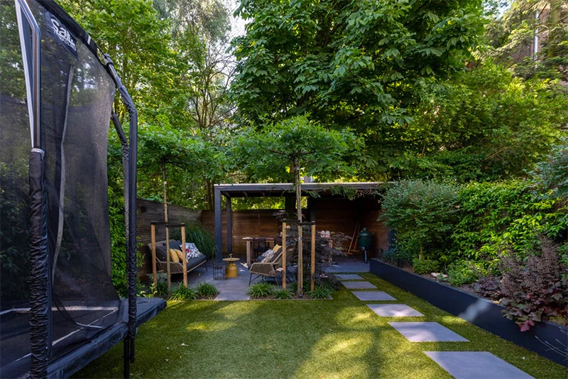 In deze mooie diepe tuin is zowel een eethoek als een zithoek achterin gecreëerd. Het looppad van grote tegels is niet alleen praktisch, het ziet er ook super mooi en strak uit.