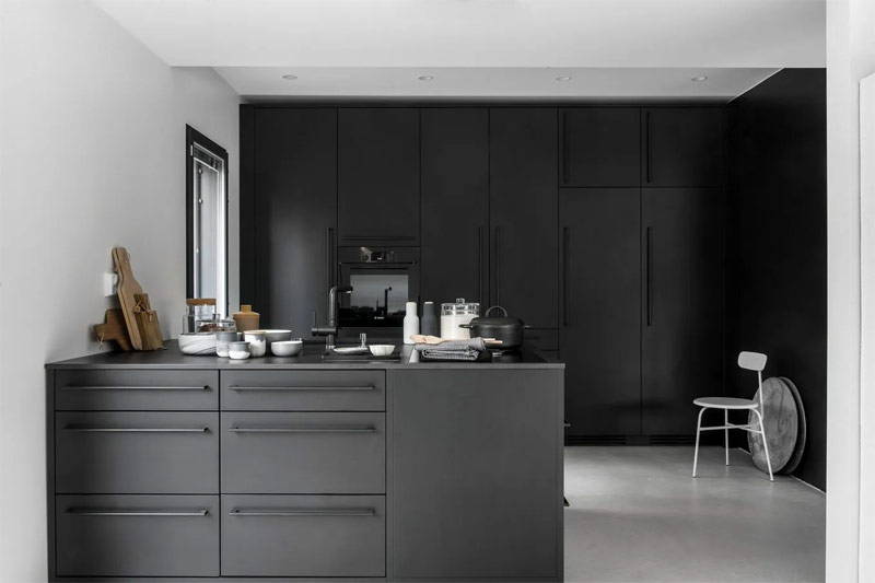 Een super stoere zwart wit keuken met zwarte keukenkasten, witte muren en plafond, en een betonlook vloer.